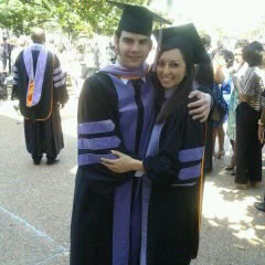 A young man and woman in graduation attire are embracing each other, smiling, and posing for a photo at an outdoor graduation ceremony.