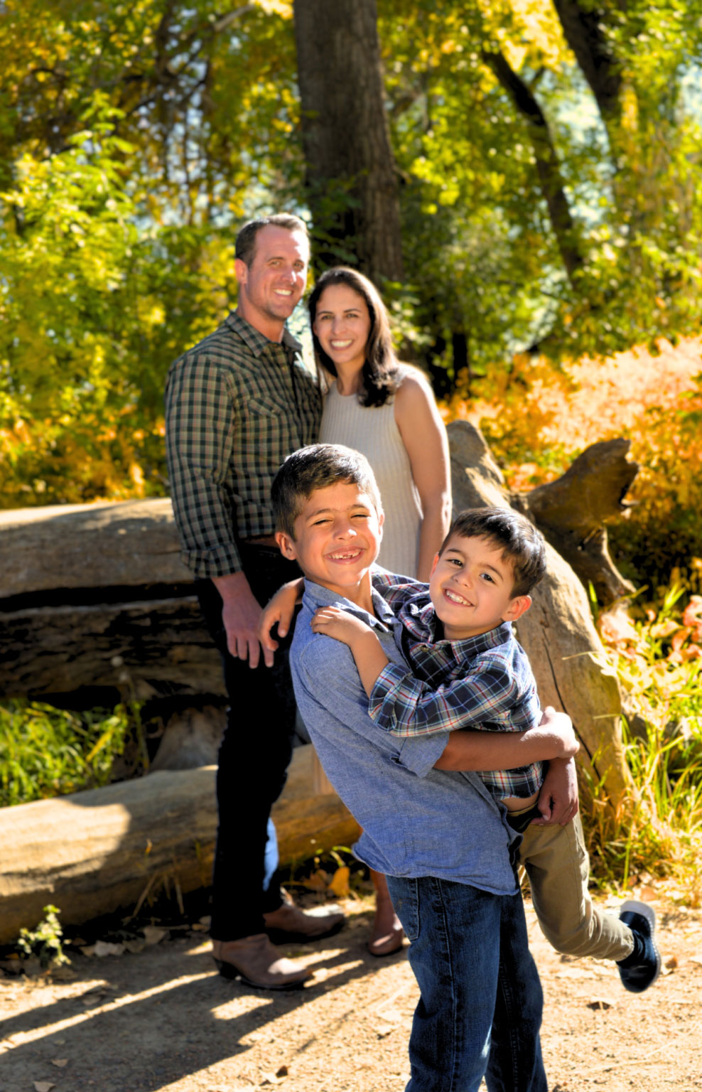 The image shows a family posing outdoors during autumn, with a man, woman, and two children smiling at the camera.