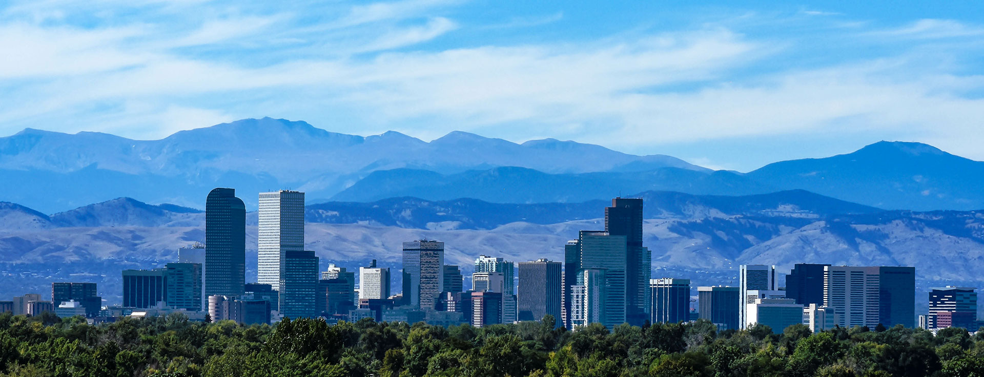 The image shows a city skyline with mountains in the background under a clear blue sky.