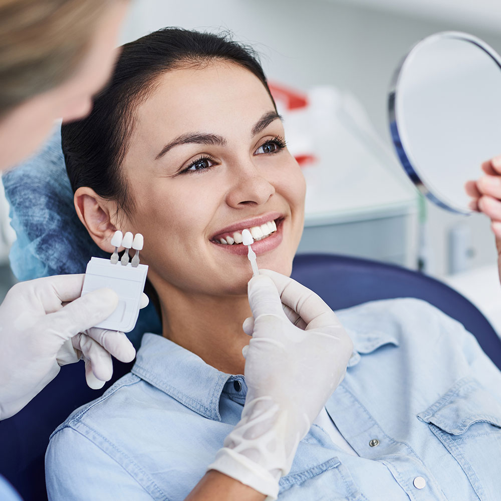 The image depicts a person receiving dental care, likely a teeth cleaning or checkup, with a dental professional assisting using a mirror and dental instruments.